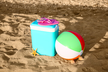 Beach cooler, inflatable ball and flip-flops on sand