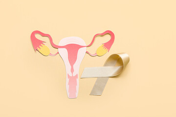 Beige ribbon with paper uterus on color background. Cancer awareness concept