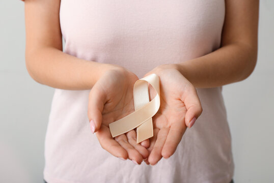 Woman with beige ribbon on light background, closeup. Uterine cancer awareness concept