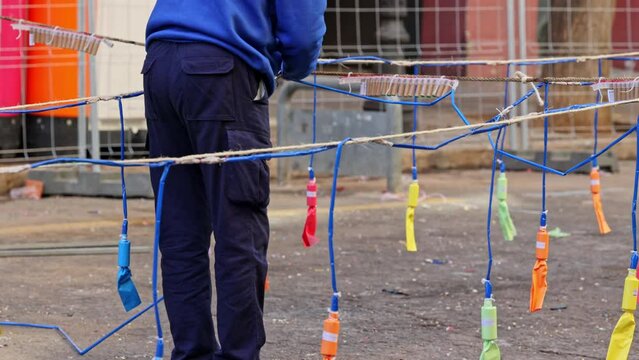 A pyrotechnician prepares a Mascleta by hanging fireworks on a city street. Colorful firecrackers bouncing on a string on a city street in front of a masklet in slow motion during Las Fallas.