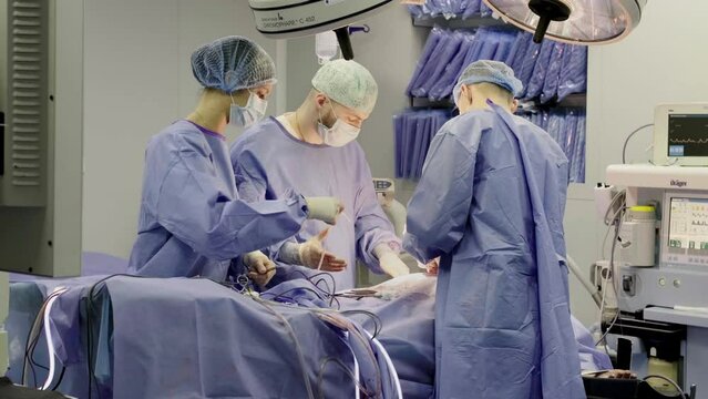 A group of professional mixed race surgeons in uniform performing an operation in the operating room using medical instruments.
