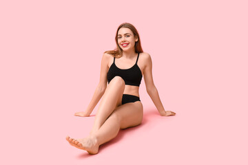 Sexy young woman in black cotton underwear sitting against pink background