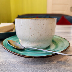 a coffee cup stands on a saucer with a small spoon on it, the background of the cafe interior