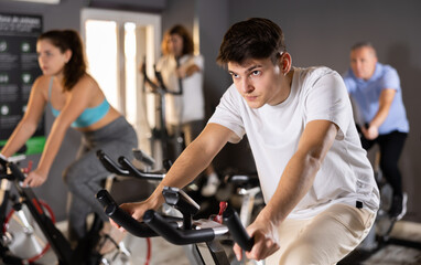 Fototapeta na wymiar Motivated young guy leading healthy active lifestyle doing cardio workout on exercise bike in gym