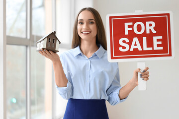Fototapeta premium Portrait of female real estate agent with house model and FOR SALE sign in new apartment