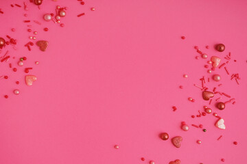 Sweet colorful sprinkles scattered on pink background