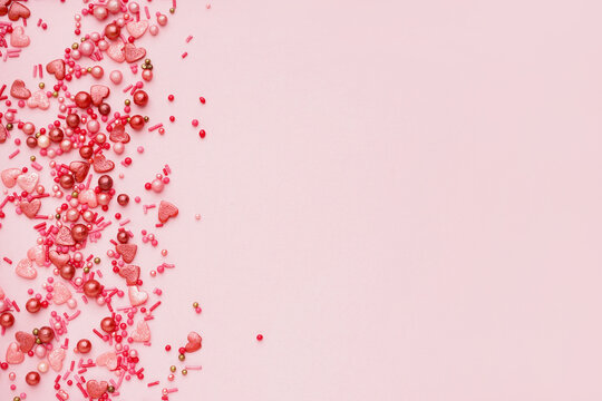 Sweet colorful sprinkles scattered on pink background