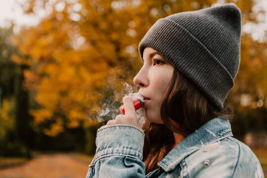 Young woman outside autumn park fall and smoking tobacco device electronic cigarette heater. Smoke and steam system with sticks inside, image with copy space. Harmful habit harm to health lungs

