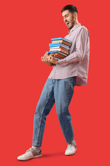 Young man with stack of books on red background
