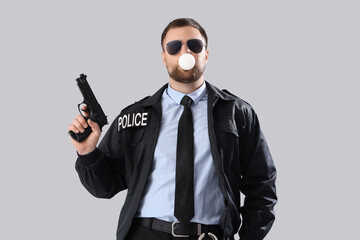 Male police officer with gun blowing bubble gum on grey background