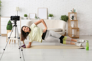 Female sports blogger training on mat while recording video at home
