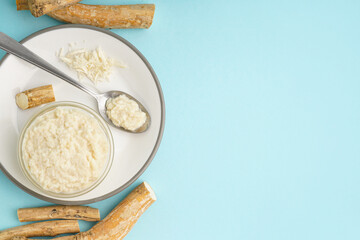 Horseradish sauce in plate with bowl, spoon and ground horseradish root on blue background. Top view
