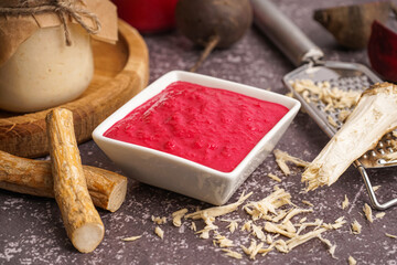 Horseradish sauce with beet in bowl and ground horseradish on grey background
