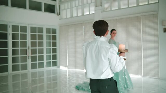 Elegant couple dancing in a bright, modern room with large windows and minimalist decor.