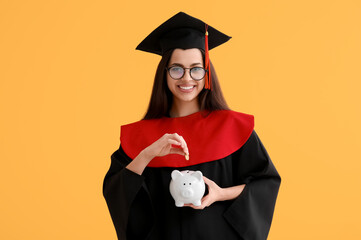 Happy female graduate with piggy bank and coin on yellow background. Tuition fees concept