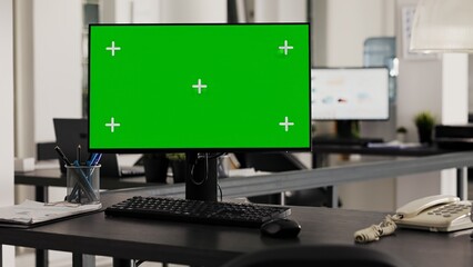 Empty desk with computer shows greenscreen on monitor, running blank mockup copyspace in business office. Workstation in open floor plan office with pc and isolated chromakey template.