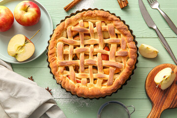 Tasty homemade apple pie with fruits, cinnamon and cutlery on green wooden background