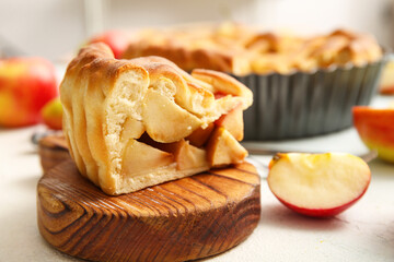 Wooden board with piece of tasty homemade apple pie on light background