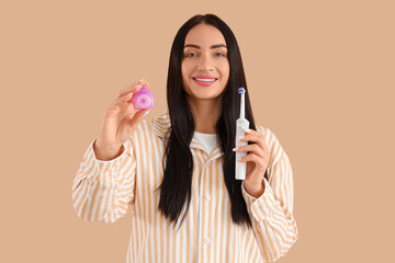 Beautiful young happy woman with dental floss and electric toothbrush on beige background