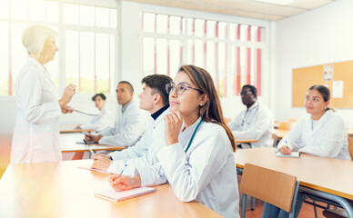Fototapeta premium Concentrated young hispanic female medical student taking notes during group lecture in university auditorium