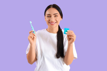 Beautiful young happy woman with dental floss and toothbrush on purple background
