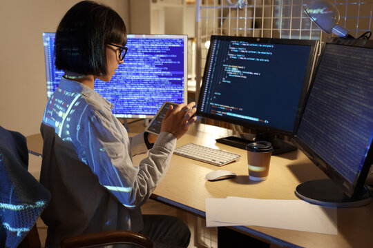 Young female programmer working with tablet computer in office at night