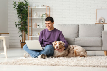 Young man with Australian Shepherd dog and laptop at home - obrazy, fototapety, plakaty