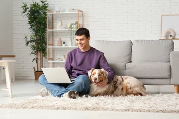 Rolgordijnen Young man with Australian Shepherd dog and laptop at home © Pixel-Shot