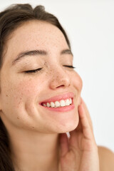 Smiling young adult woman with freckles touching face enjoying fresh clean smooth skin advertising...