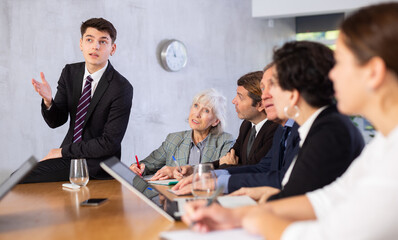 Young confident manager sitting on table and conducting work meeting with colleagues. Concept of modern informal communication in office