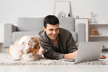 Young man with Australian Shepherd dog using laptop on floor at home