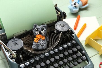 Vintage typewriter with paper and knitted toys on green background