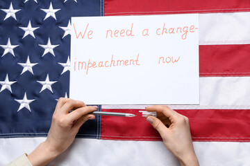 Woman writing text WE NEED A CHANGE - IMPEACHMENT NOW on picket poster against USA flag