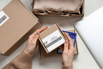 Female hands holding cardboard package with barcode and label at white table