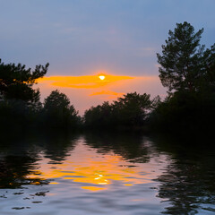 Fototapeta na wymiar tree silhouette on lake coast at the sunset