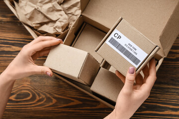 Woman holding cardboard package with label and barcode at wooden table