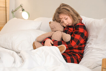Adorable little girl in pajamas with teddy bear sleeping in bed