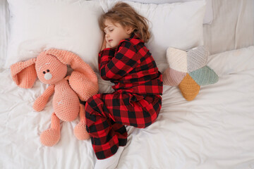 Adorable little girl with plush bunny sleeping in bed