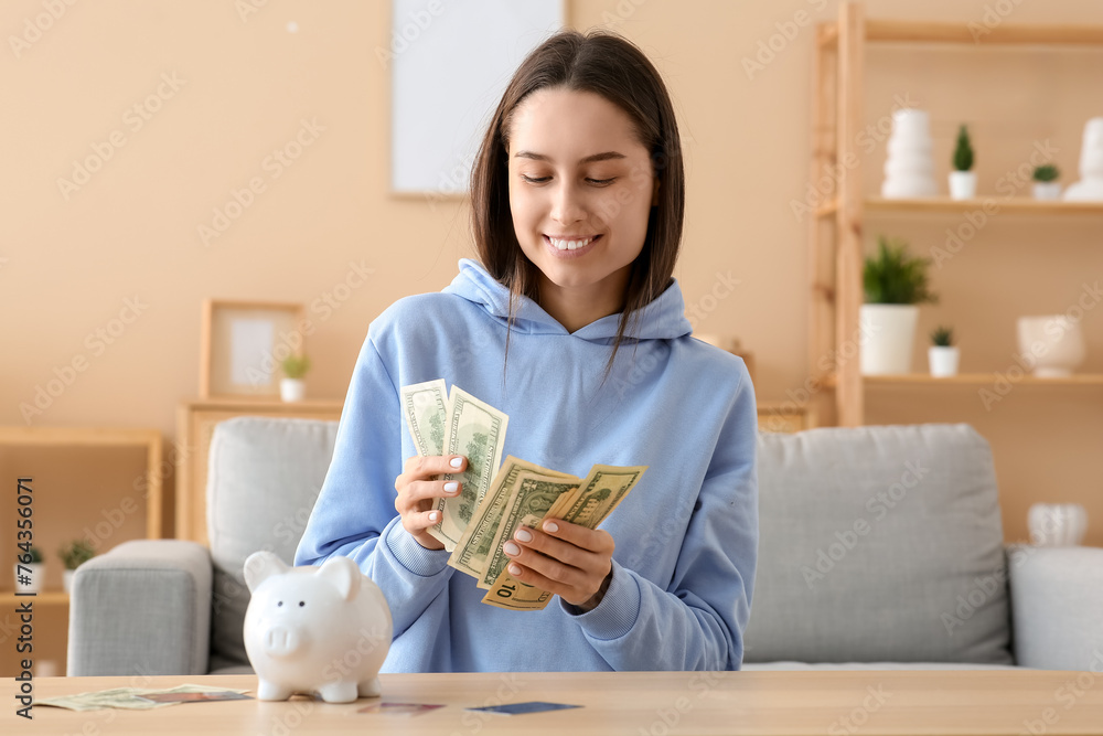 Sticker Pretty young woman with piggy bank and credit cards counting money at home