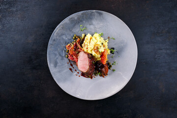 Traditionell gebratenes Wildhasen Rücken Filet mit Pflaumen, Kapern und Kartoffelsalat in Rotweinjus serviert als Draufsicht auf einem Nordic Design Teller mit Textfreiraum