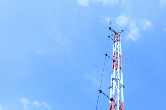 Meteorological measurement instrument pole. Base station with anemometer device Temperature and humidity on metal pole with lightning rod against thin cloudy sky in bottom view and selective focus.