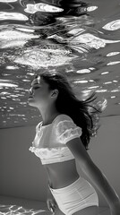 Surreal underwater portrait in monochrome: black and white image of a young woman floating gracefully, with light patterns on water surface above