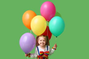 Fototapeta na wymiar Cute little girl in clown costume with balloons on green background