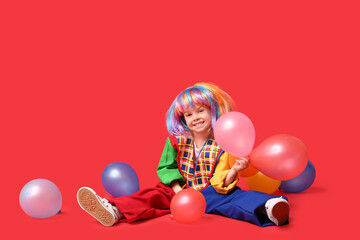 Fototapeta na wymiar Smiling girl in clown costume and colorful wig with balloons on red background