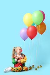 Fototapeta na wymiar Cute girl in clown costume and balloons on blue background