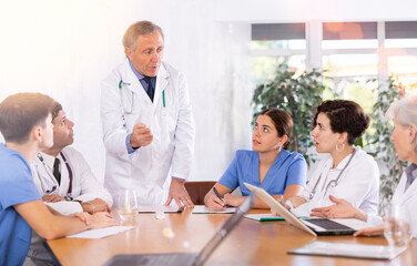 Focused experienced elderly head doctor conducting medical council with male and female colleagues...