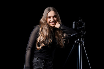 Portrait of female photographer with modern camera on tripod against black background
