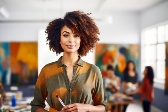 Portrait of Adult African American female art teacher with a brush in hand in art studio. Students and creative canvas on class background. Concept of artistry and guidance. Copy space