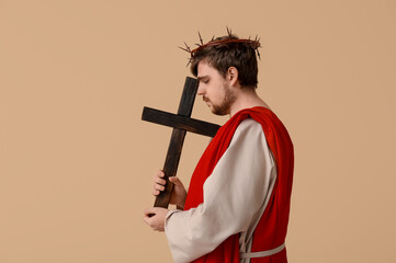 Man in Jesus robe and crown of thorns with wooden cross on beige background