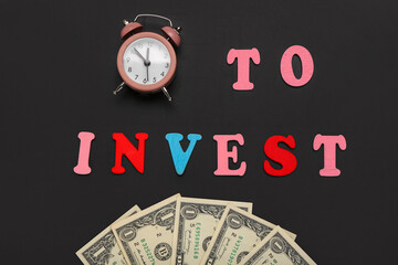 Text TO INVEST alarm clock and dollar banknotes on black background. Top view